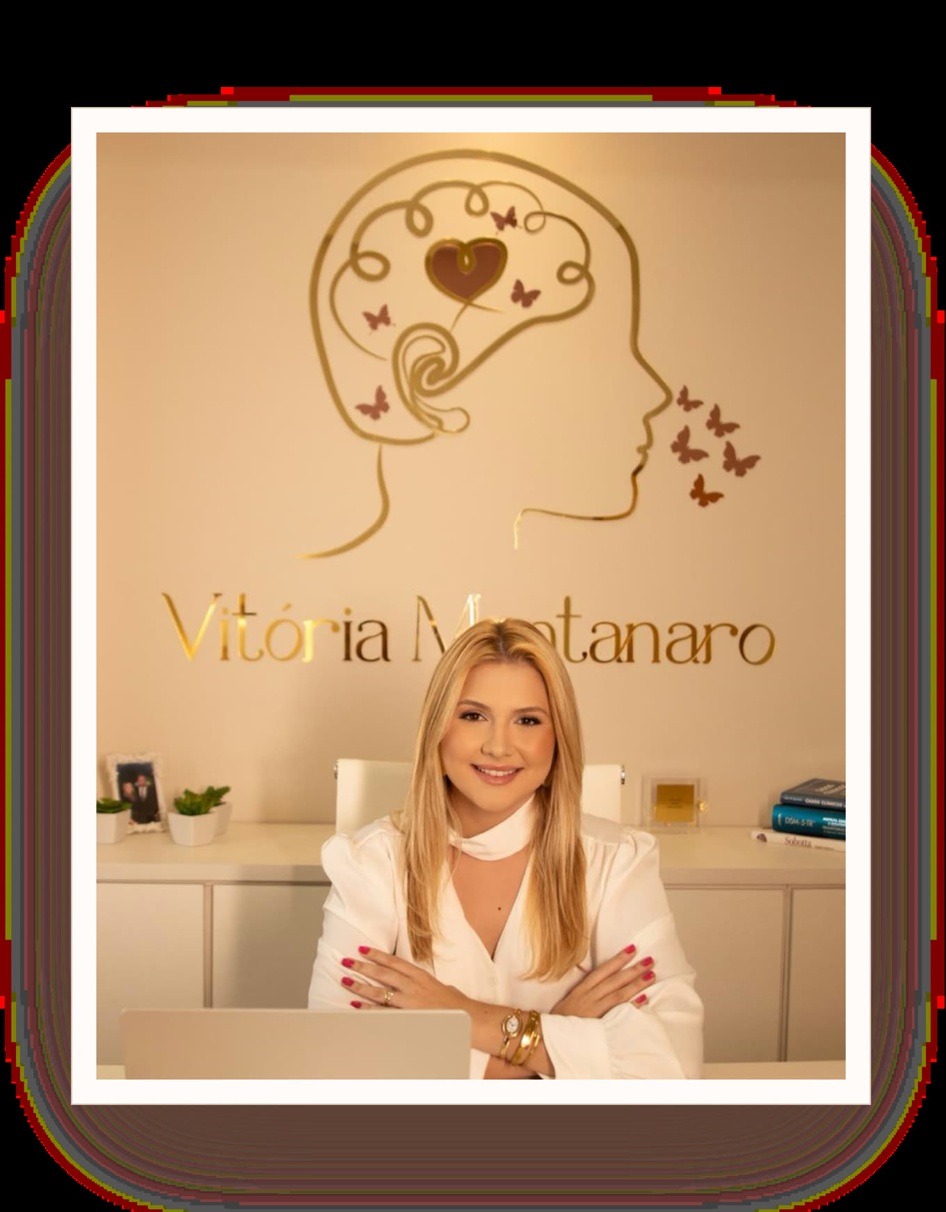 Vitória Montanaro sentada à mesa do consultório, sorrindo, com o símbolo da marca na parede ao fundo.